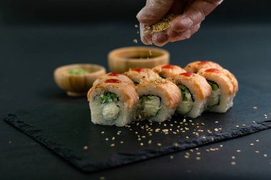 Yakın çekim manzara haddeleme suşi hazırlama işleminin. Elinde eldiven lezzetli taze rulo bir susam ile süsle. Koyu arka plan