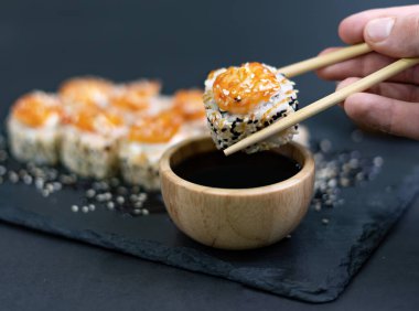 Closeup of Shrimp sushi held with bamboo chopsticks. Shrimp sushi with sesame on blackground. Japanese sushi