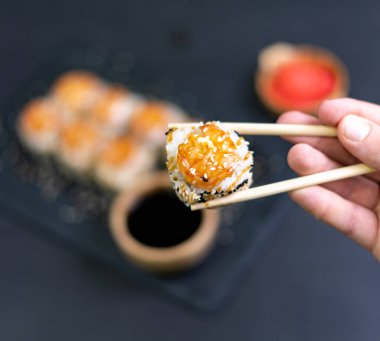 Closeup of Shrimp sushi held with bamboo chopsticks. Shrimp sushi with sesame on blackground. Japanese sushi