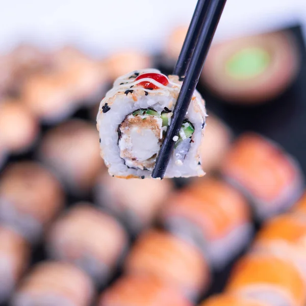 Japanese cuisine. One peace of sushi roll in black chopsticks
