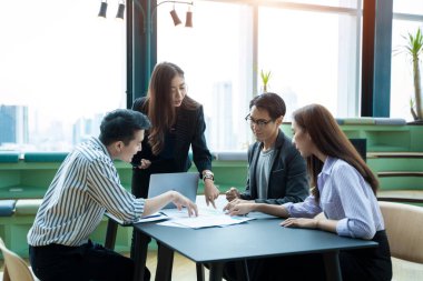Bir grup iş ortağı ofis odasında yeni projeyi tartışıyor, fikri açıklıyor ve çalışma planını gösteriyor..