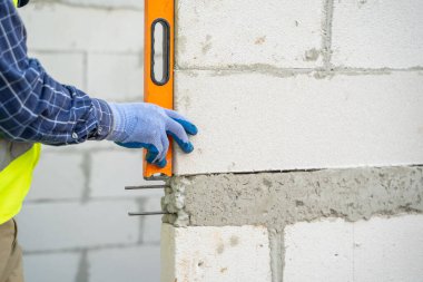 Engineer measures the work out wall lightweight concrete blocks with a level at construction site.