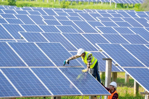 Two electrician workers in reflective vests and hard hats working and talking about installation of new solar panels.