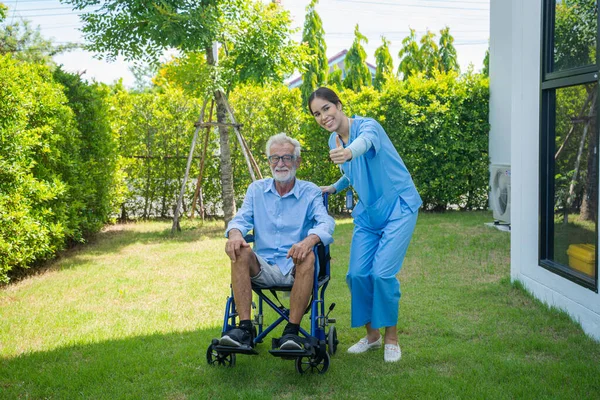 Nurses rehab exercises and take care senior disabled man on wheelchair.Providing medical assistance to impaired senior adult.