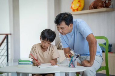 Baba çocuklara ev ödevi öğretiyor, neşeli baba ve Asyalı küçük çocuk evde resim yapıyor..
