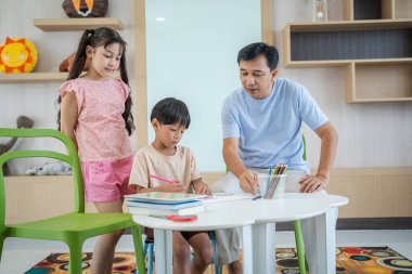 Anne ve baba, çocuklara ev ödevlerini evde yapmayı öğretiyor..