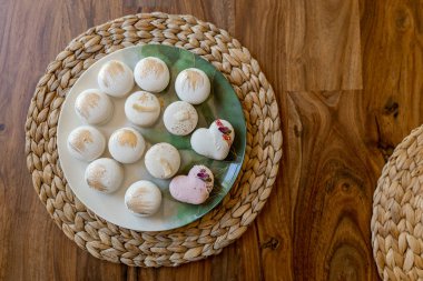 White and pink macarons lie on a plate on a wooden table. Delicious light cookies on a brown background. Bakery. Valentine's Day background