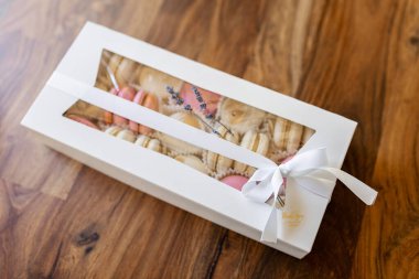 Beyaz bir kutuda güzelce paketlenmiş bir hediye. Mutfaktaki ahşap masada beyaz bir hediye kutusunda pembe ve beyaz makaronlar..