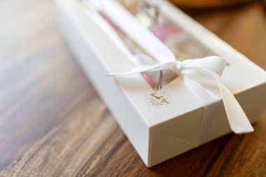 Beyaz bir kutuda güzelce paketlenmiş bir hediye. Mutfaktaki ahşap masada beyaz bir hediye kutusunda pembe ve beyaz makaronlar..