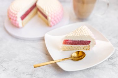 White and pink cake on a plate on a light marble table and a glass coffee mug. Background for Valentine's Day