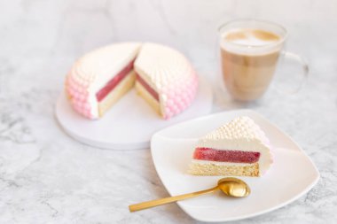 White and pink cake on a plate on a light marble table and a glass coffee mug. Background for Valentine's Day