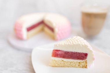 White and pink cake on a plate on a light marble table and a glass coffee mug. Background for Valentine's Day
