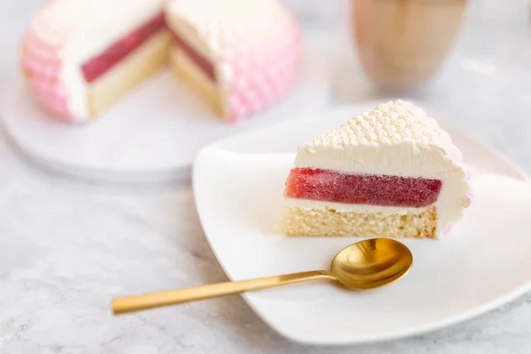White and pink cake on a plate on a light marble table and a glass coffee mug. Background for Valentine's Day