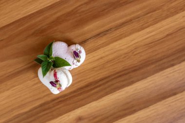 Beautiful tender delicious pastries with a green leaf on a wood brown background. White and pink macaroons on a table. Valentines Day background