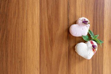 Beautiful tender delicious pastries with a green leaf on a wood brown background. White and pink macaroons on a table. Valentines Day background