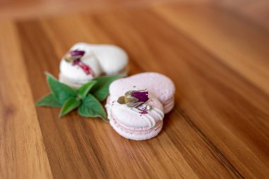Beautiful tender delicious pastries with a green leaf on a wood brown background. White and pink macaroons on a table. Valentines Day background