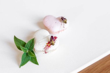 Hafif arka planda yeşil yapraklı güzel, lezzetli hamur işleri. Beyaz bir tuvalde beyaz ve pembe badem kurabiyeleri. Sevgililer Günü arkaplanı