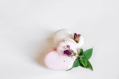 Hafif arka planda yeşil yapraklı güzel, lezzetli hamur işleri. Beyaz bir tuvalde beyaz ve pembe badem kurabiyeleri. Sevgililer Günü arkaplanı