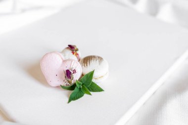 Hafif arka planda yeşil yapraklı güzel, lezzetli hamur işleri. Beyaz bir tuvalde beyaz ve pembe badem kurabiyeleri. Sevgililer Günü arkaplanı