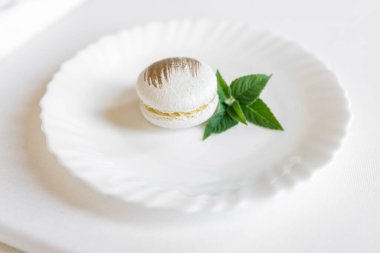 Beyaz arka planda yeşil nane yaprağı olan beyaz makaronlar. Lezzetli ve güzel hamur işleri. Şekerlemeler için arka plan