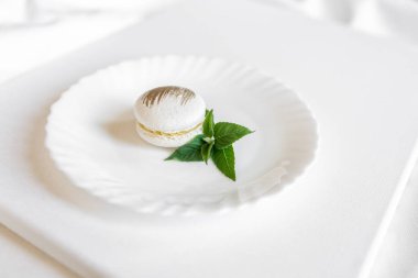 Beyaz arka planda yeşil nane yaprağı olan beyaz makaronlar. Lezzetli ve güzel hamur işleri. Şekerlemeler için arka plan