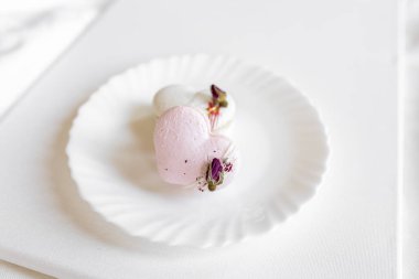 Pembe kalp şeklinde bir pasta beyaz bir tabakta, arka planda yatar. Beyaz bir tuval üzerinde hafif badem kurabiyeleri. Sevgililer Günü arkaplanı