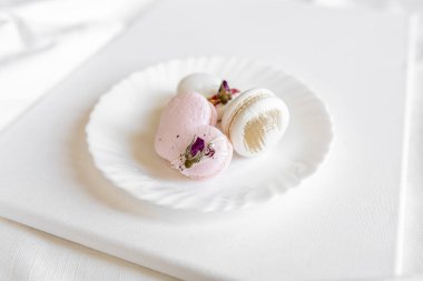 Pembe kalp şeklinde bir pasta beyaz bir tabakta, arka planda yatar. Beyaz bir tuval üzerinde hafif badem kurabiyeleri. Sevgililer Günü arkaplanı