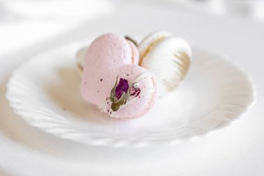 Pembe kalp şeklinde bir pasta beyaz bir tabakta, arka planda yatar. Beyaz bir tuval üzerinde hafif badem kurabiyeleri. Sevgililer Günü arkaplanı