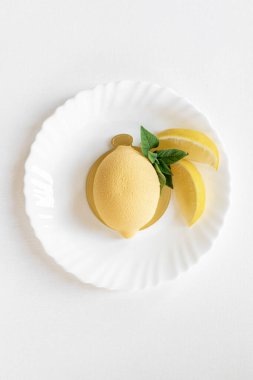 Yeşil nane yaprağı ve beyaz arka planda gerçek limon dilimleri olan limon şeklinde kremalı pasta. Lezzetli ve güzel hamur işleri. Şekerlemeler için arka plan