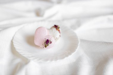 Pembe kalp şeklinde bir pasta beyaz bir tabakta, arka planda yatar. Beyaz bir tuval üzerinde hafif badem kurabiyeleri. Sevgililer Günü arkaplanı