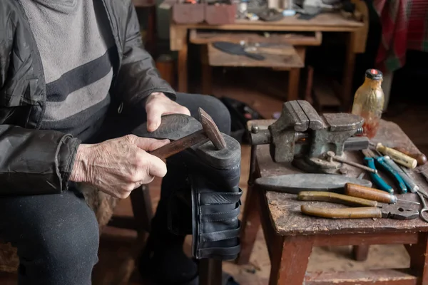 Emekli bir ayakkabıcı ayakkabıları tamir eder. Yanında bir sürü enstrüman var..