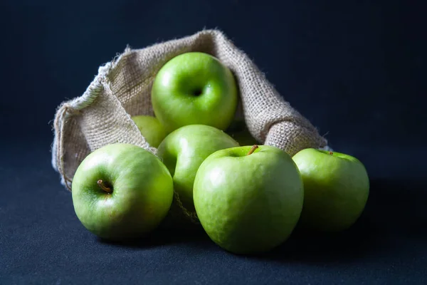 Yeşil elmalar çantada ve masada. Karanlık bir arka planda.