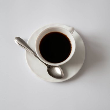 Masanın üzerinde bir fincan fincan fincan kahve var. Yanında bir kaşık var. Beyaz arkaplanda.