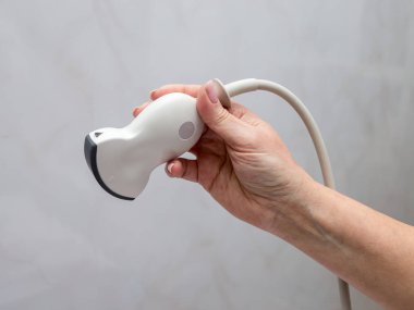 Doktor elinde bir ultrason sondası tutuyor. Gri bir arkaplanda.