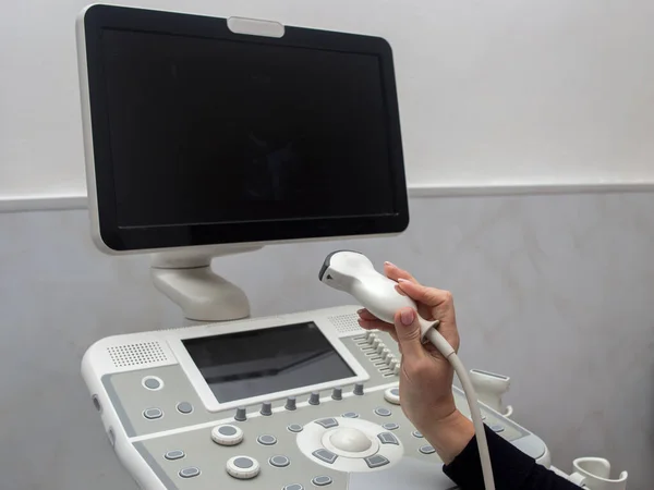 Doktor elinde bir ultrason sondası tutuyor. Bir ultrason makinesinin arka planında.