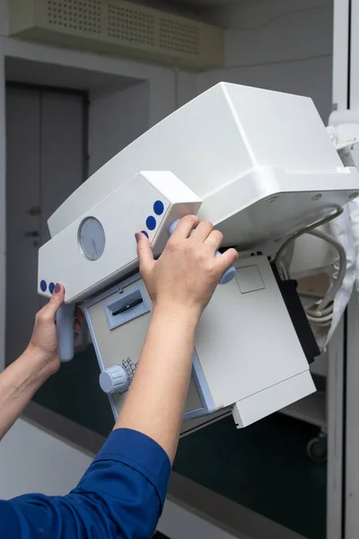 Radyoloji uzmanı röntgen cihazını hazırlıyor. Gri bir duvarın arkasında.