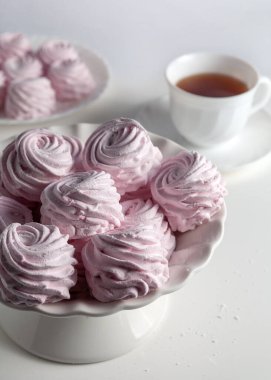 Masanın üzerindeki vazoda bir şekerleme var. Onun yanında bir fincan çay var. Beyaz bir arka planda. Seçici odak.