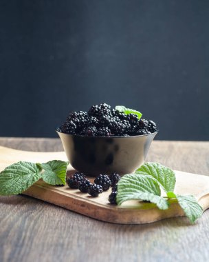 There is a blackberry in a bowl on the table. There are green leaves near her.