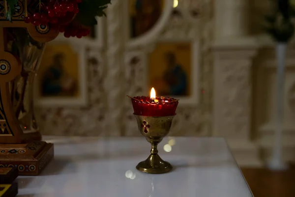 There is a burning candle on the table in the church. Horizontal frame.