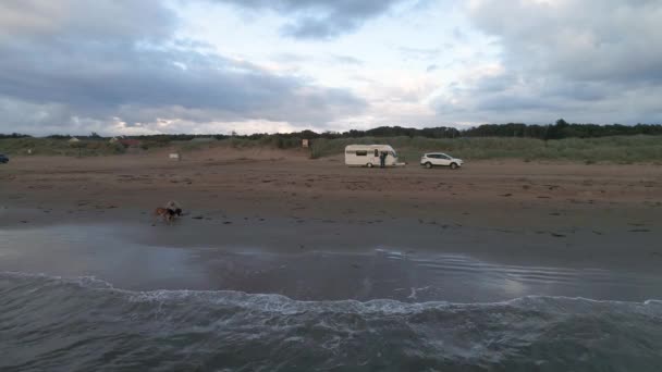 50fps Antenne Sonnenuntergang Paar mit Hund auf Outdoor-Urlaub Wohnwagen Campingplatz Camper am Strand von Melby, Schweden am Meer — Stockvideo