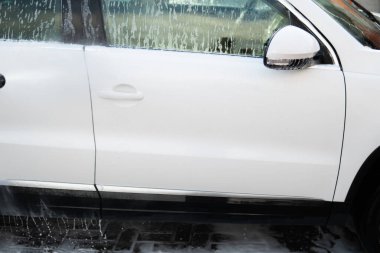 Manual car wash outside. Close up. High Pressure Water. Manual car wash with white soap, foam on the body. Cleaning Car Using Washing with soap.