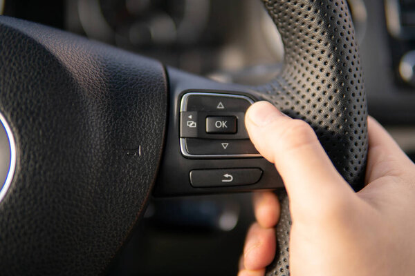 Hands of a driver on car steering wheel. Dashboard. Green field countryside landscape along the road. Beautiful blue sunny sky. Windshield and side window view. Man steers auto