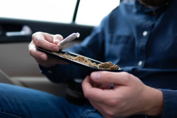 stock image flowers of cannabis. grinder and shredded cannabis joint packet of weed on a car background close up marijuana joint in hand bud