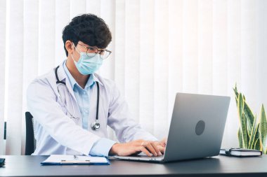 Doktor ofiste oturmuş, maske takarken dizüstü bilgisayarla uğraşıyordu..
