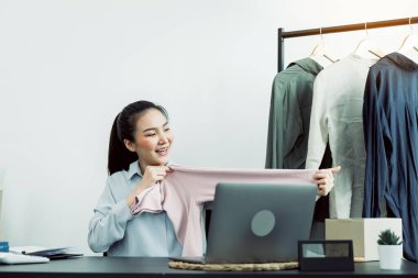 Genç Asyalı girişimciler, müşterilerin internetten izlemesi için oranlarını karşılaştırmak üzere gömlek seçiyorlar..