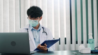 Doktor ofiste oturmuş, maske takarken dizüstü bilgisayarla uğraşıyordu..