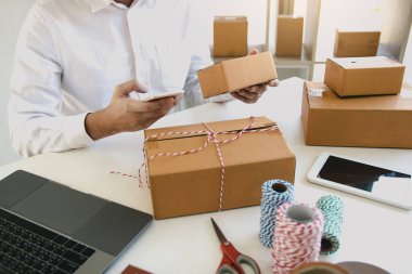 Asyalı genç adam evdeki siparişleri kontrol etmek için akıllı telefon kullanıyor..