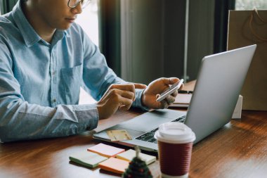 Adamın elleri akıllı telefonlar tutuyor ve dizüstü bilgisayar kullanarak ürün satın almak için web sitelerine giriyorlar..