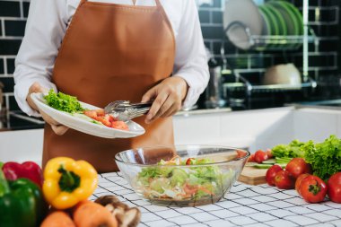Asyalı kadın salatayı salata kasesine koymaya hazırlanan malzemeleri döküyor..