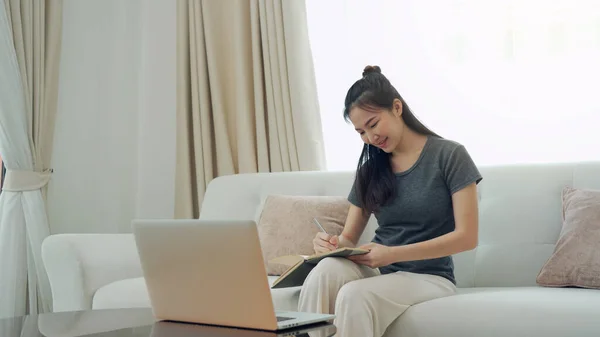 Mujer Asiática Sienta Sofá Mientras Toma Notas Pantalla Computadora Mientras —  Fotos de Stock